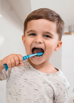 A child with brown hair is brushing their teeth with a blue toothbrush while standing in a bright bathroom. No landmarks or historical buildings visible.