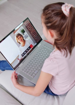 A child is video chatting with a person on a laptop. The person appears on the laptop screen, engaged in conversation.