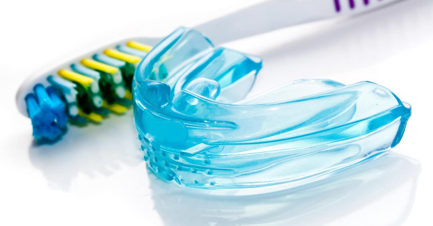 A toothbrush and a blue dental mouthguard are placed on a white surface, emphasizing dental hygiene items. No landmarks or historical buildings present.