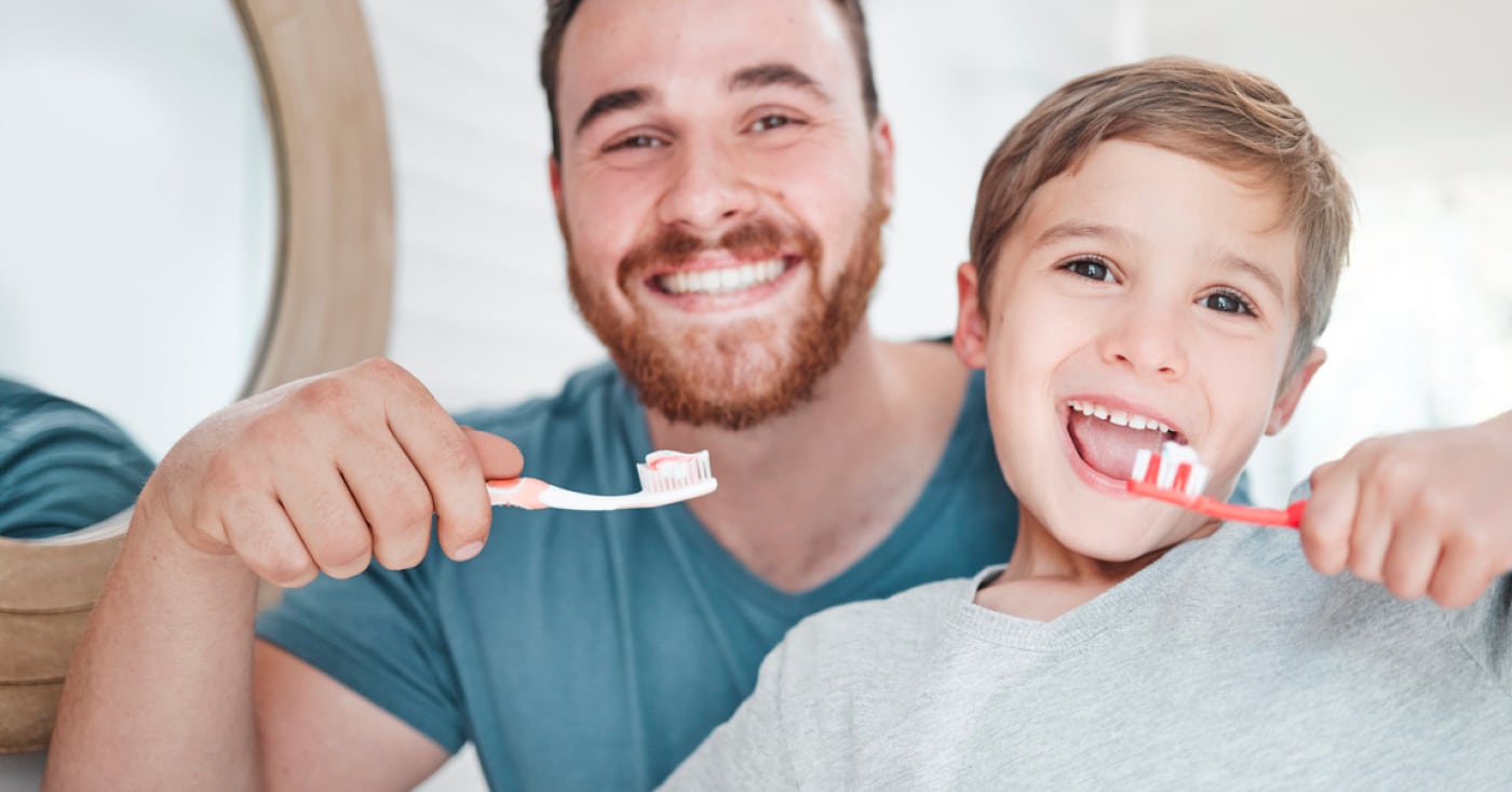 A smiling person and child are brushing their teeth together, posing in front of a mirror, creating a joyful and healthy bonding moment.
