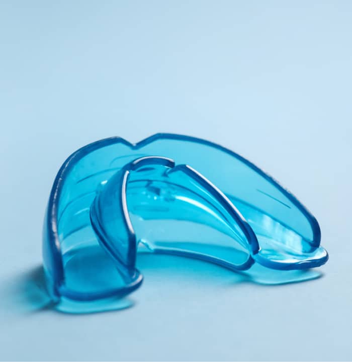 A close-up of a blue plastic mouthguard against a light blue background, used for dental protection during sports or orthodontic treatment.